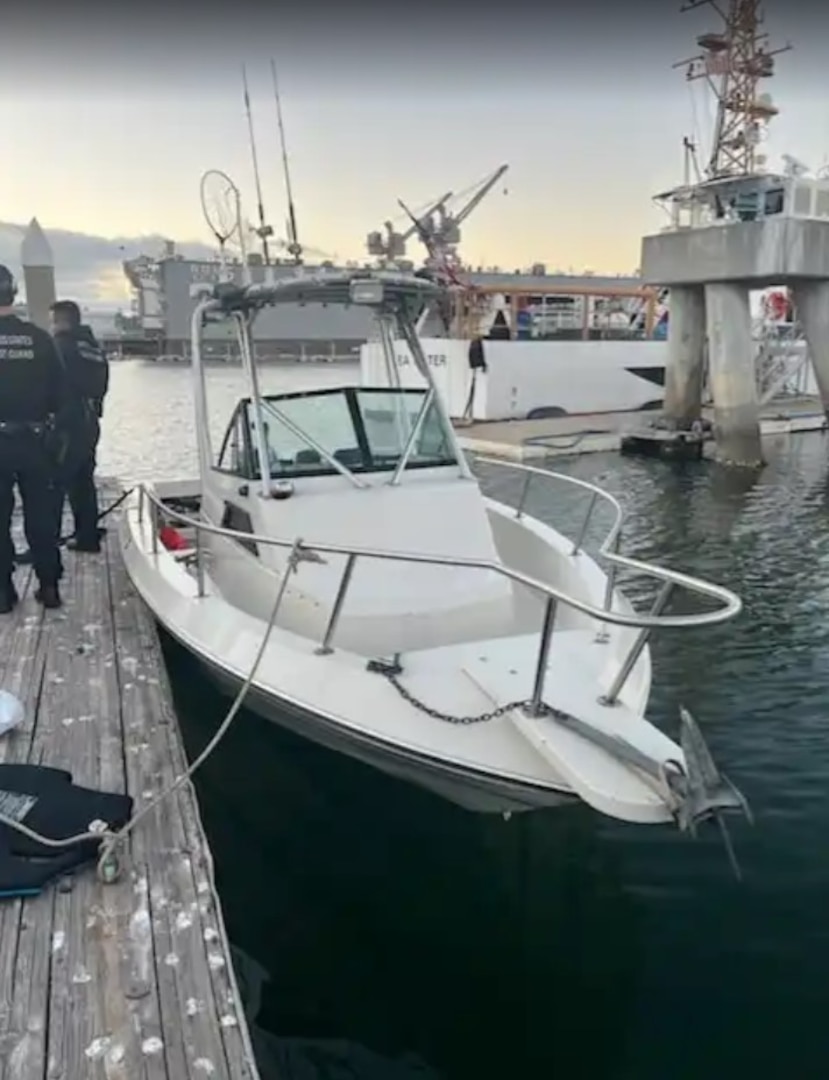 Two Coast Guardsmen are seen standing on a pier next to a white 20-foot center console boat.
