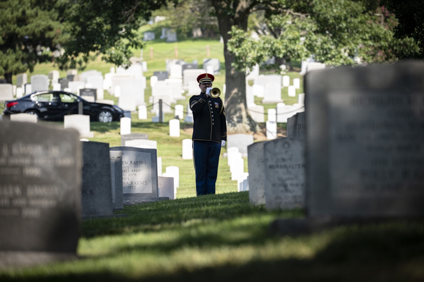 A man dressed in a military uniform plays a bugle in a cemetery.