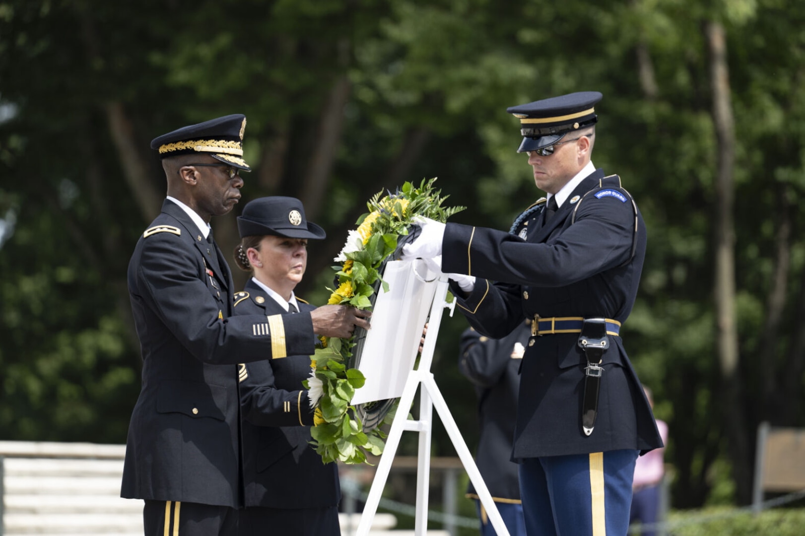 Two men and a woman dressed in military uniforms place a wreath and a woman dressed in military uniforms place a wreath on an easel.