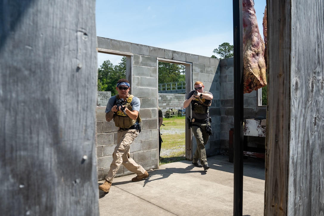 Two men holding fake guns are training to sweep a room