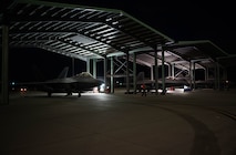 Three F-22 Raptors under hangars at night.