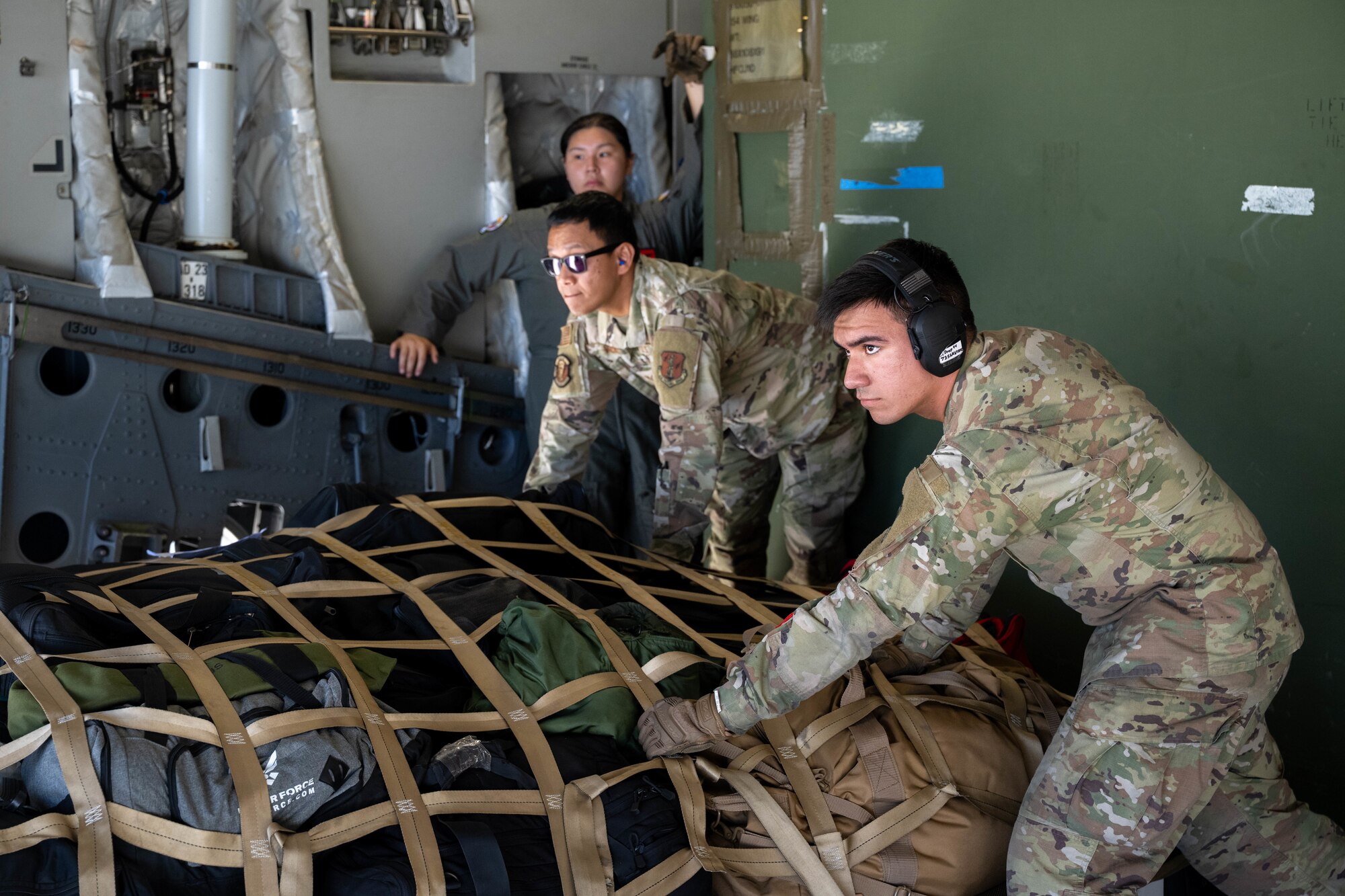 Three Airmen pushing netted cargo inside of a C-17.