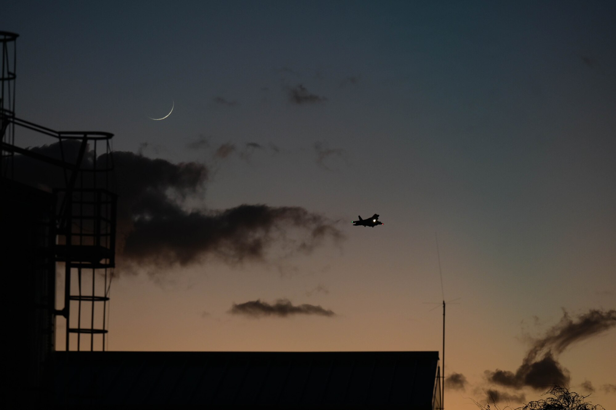 An F-22 landing during the sunset with a moon in the background.