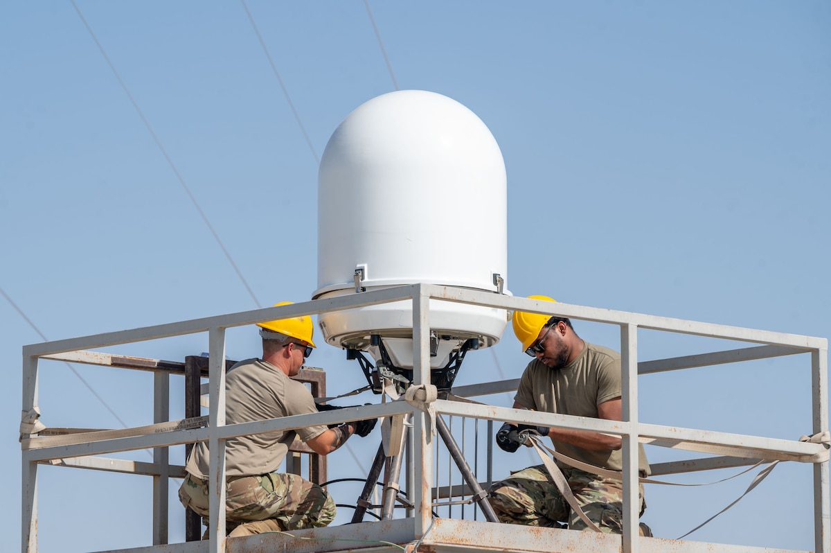 A PDR sits on a platform mid-frame as two Airmen are on either side working on its installation