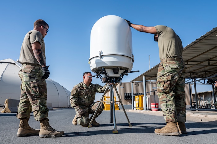 a PDR sits mid-frame as three Airmen surround it in preparation for installation