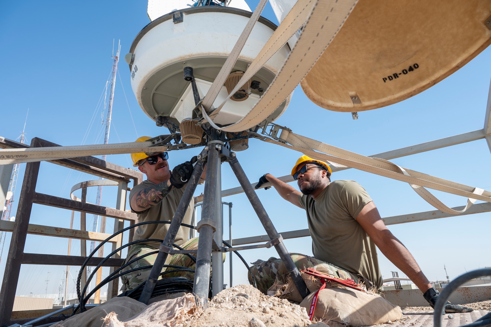 Master Sgt. Lancaster and Senior Airman Washington kneel beside a PDR as they install it