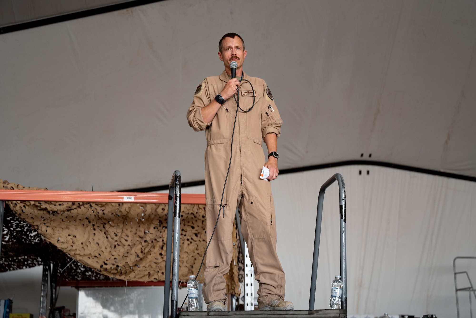 An Airman stands on a platform holding a microphone