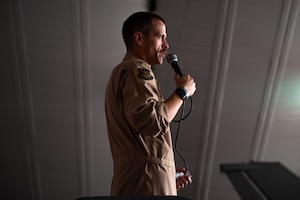 An Airman stands on a platform holding a microphone