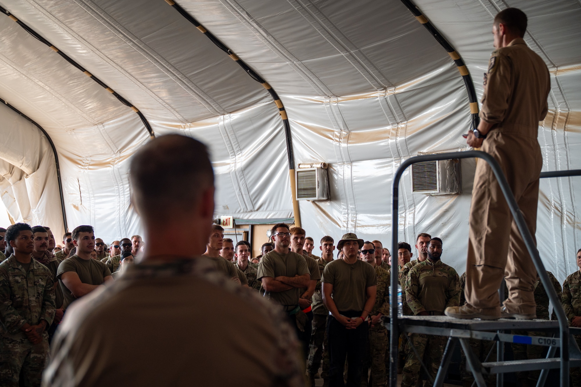 An Airman stands on a platform while a crowd of Airmen gather around