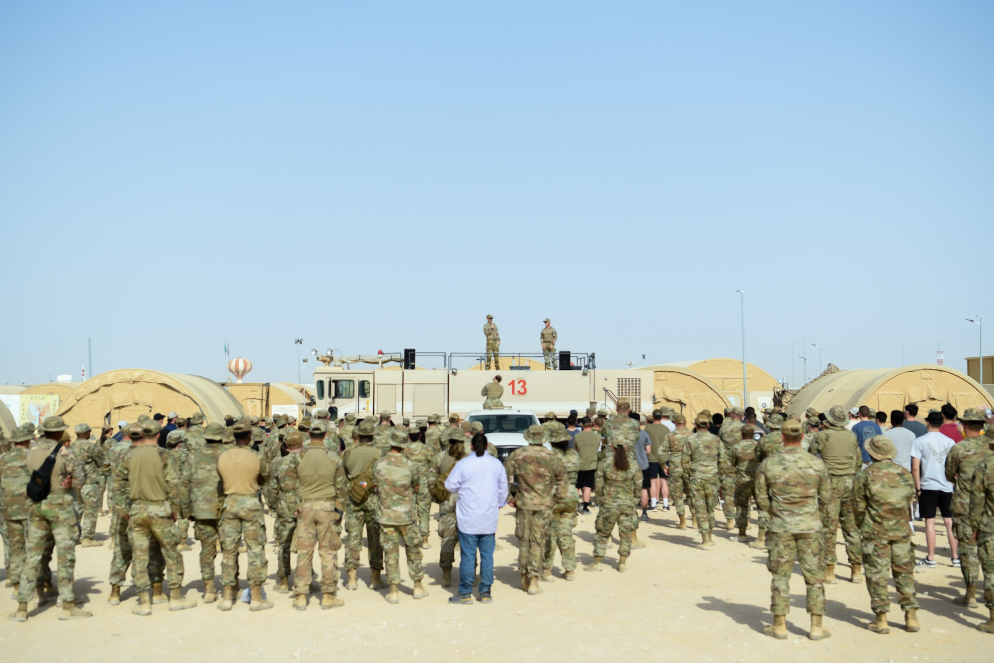 Two Airmen stand on a fire truck in front of a crowd of uniformed personnel