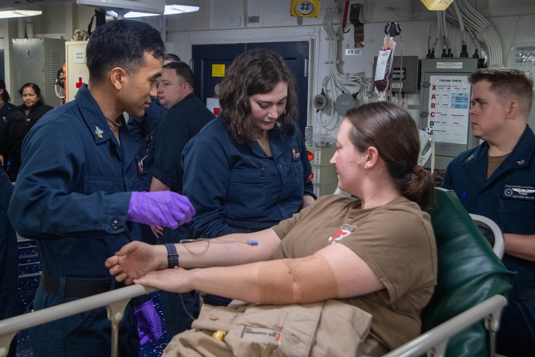 250724-N-TW227-1052 CORAL SEA (July 24, 2025) U.S. Navy Hospital Corpsman 1st Class Joshua Ayeras, from San Jose, California, left and Hospital Corpsman 3rd Class Madison Lagano, from Charlottesville, Virginia, center, assigned to Fleet Surgical Team 7, conduct blood draw training in the medical bay of the forward-deployed amphibious assault ship USS America (LHA 6), flagship of the America Strike Group, during Talisman Sabre 25, July 24. Talisman Sabre is the largest bilateral military exercise between Australia and the United States advancing a free and open Indo-Pacific by strengthening relationships and interoperability among key allies and partners, while enhancing our collective capabilities to respond to a wide array of potential security concerns. (U.S. Navy photo by Mass Communication Specialist 3rd Class Kenneth Melseth)