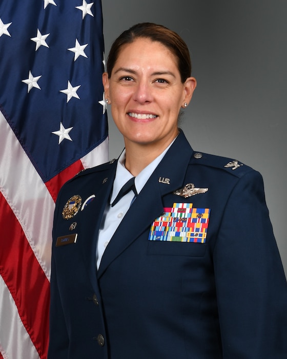 Woman in military uniform smiling at camera with U.S. flag in the background
