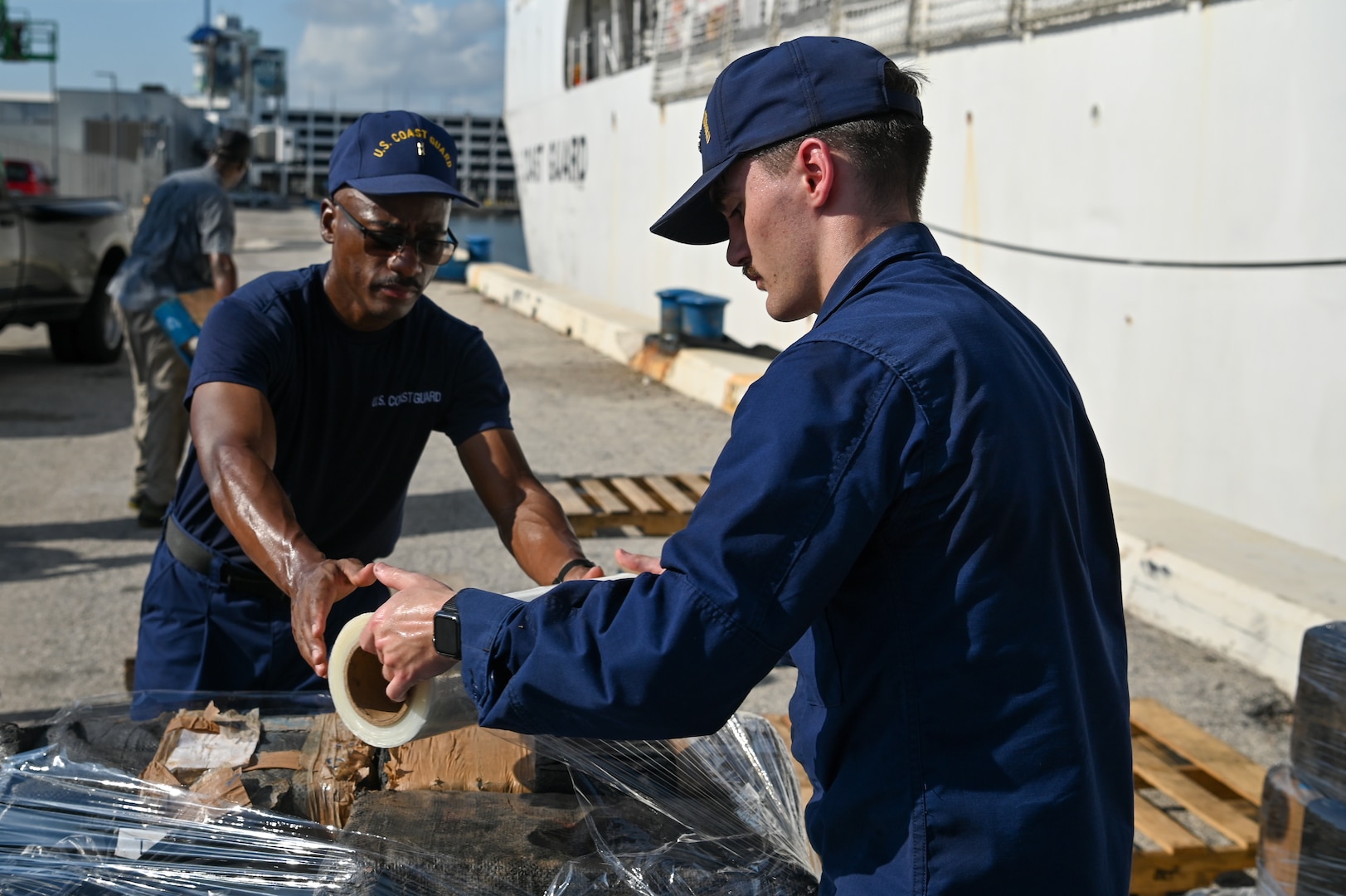 The crew of the Coast Guard Cutter Tahoma wrapping bales of cocaine on the pier at Port Everglades, Florida, July 29, 2025. Interdicted contraband is transferred to partner agencies for destruction. (U.S. Coast Guard photo by Petty Officer 3rd Class Nicholas Strasburg)