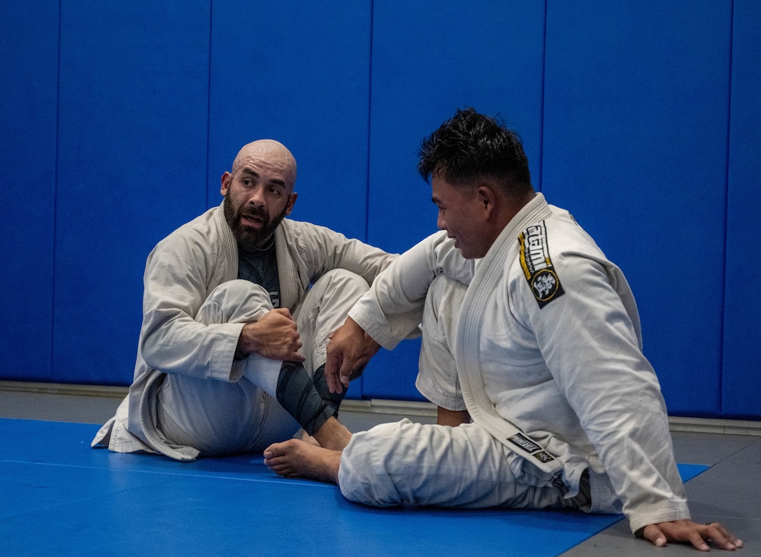 Two men sit on a blue mat.