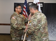 Capt. Justine Juan, left, incoming Headquarters and Headquarters Detachment commander for U.S. Army Medical Logistics Command, receives the unit’s guidon from AMLC Commander Col. Marc Welde during a change of command ceremony July 18 at Fort Detrick, Maryland. The ceremony also served to recognize outgoing commander, Maj. Shirly Rivera.