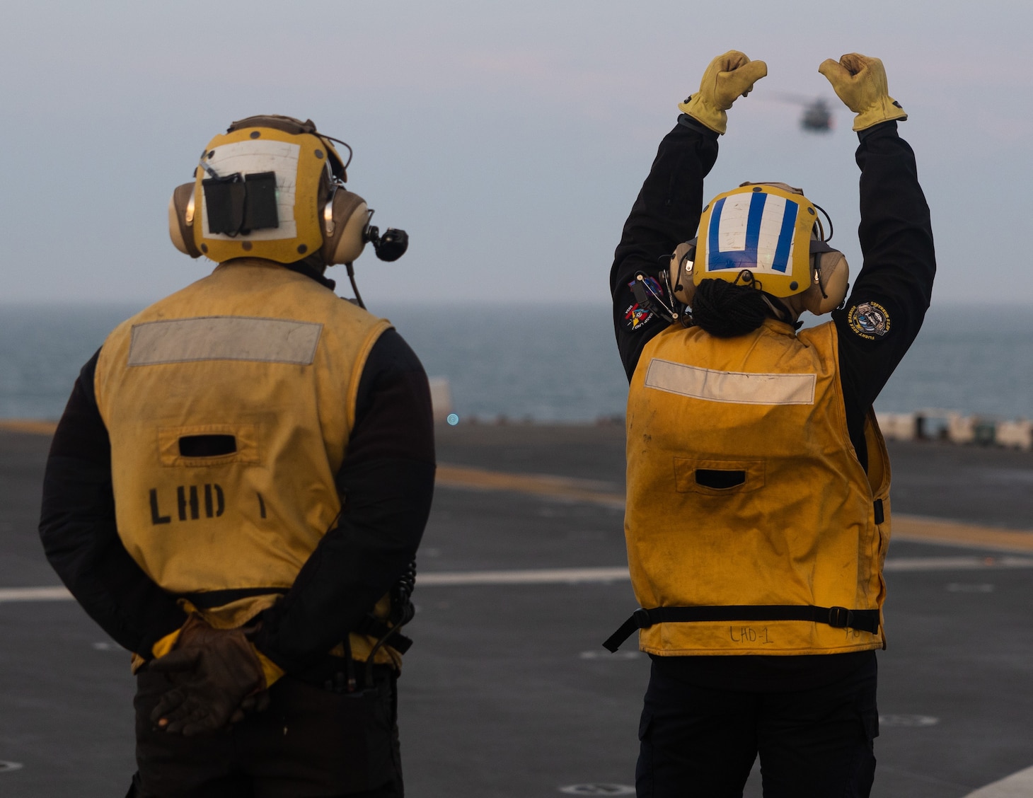 Aviation Boatswain’s Mate (Handling) 3rd Class Gerald Manful, left, and Aviation Boatswain’s Mate (Handling) Airman Rigio Carpea, both assigned to the amphibious assault ship USS Wasp (LHD 1), signal to a pilot aboard an MH-53E Sea Dragon, assigned to the “Blackhawks” of Helicopter Mines Countermeasures Squadron 15 (HM-15), to land on the ship’s flight deck during flight operations, April 5, 2025. Wasp is underway conducting routine operations in the Atlantic Ocean.