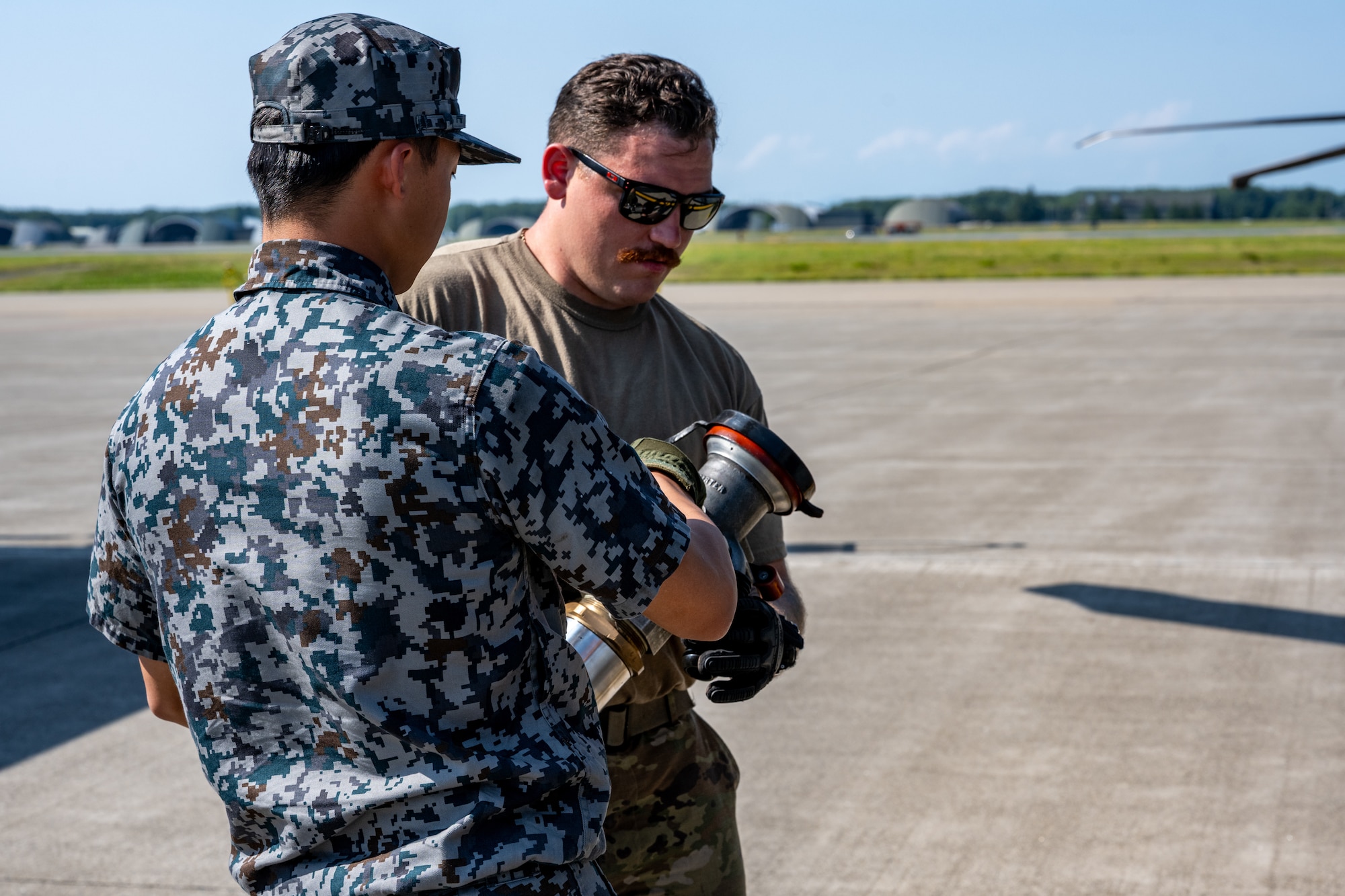 Japan Air Self-Defense Force Staff Sgt. Yuui Asanuma, 3rd Air Wing petroleum, oil, and lubricant technician, hands a fuel line to U.S. Air National Guard Senior Airman Brenden Wassmer, 106th Rescue Wing helicopter crew chief, during exercise Resolute Force Pacific (REFORPAC) 2025 at Misawa Air Base, Japan, July 16, 2025.