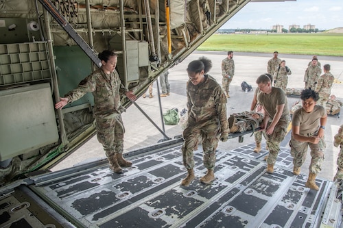 Servicemembers carry personnel on gurneys aboard an aircraft.