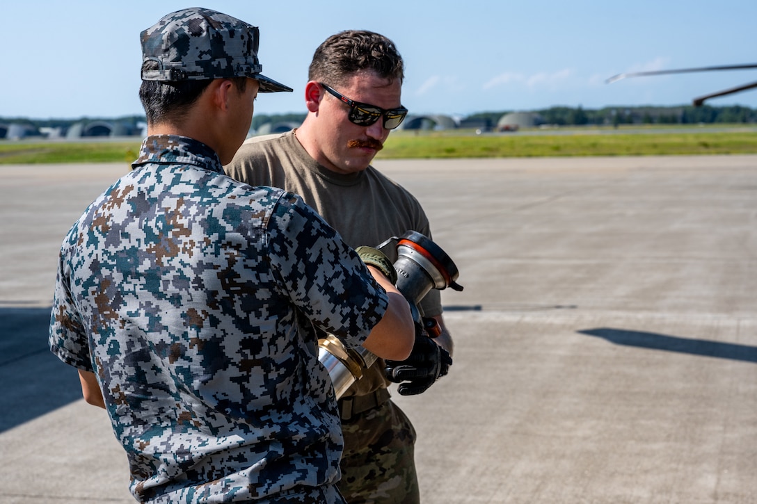 Japan Air Self-Defense Force Staff Sgt. Yuui Asanuma, 3rd Air Wing petroleum, oil, and lubricant technician, hands a fuel line to U.S. Air National Guard Senior Airman Brenden Wassmer, 106th Rescue Wing helicopter crew chief, during exercise Resolute Force Pacific (REFORPAC) 2025 at Misawa Air Base, Japan, July 16, 2025.