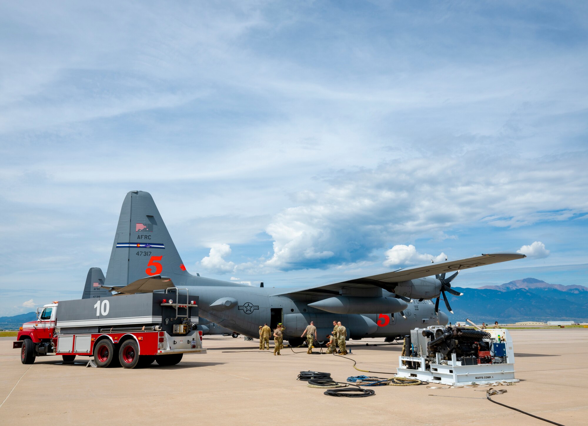 A fire truck, a military aircraft, a piece of equipment and a military crew in the center on the flightline.