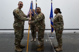 U.S. Air Force Lt. Col Sande C. Penuliar, middle, 379th Expeditionary Logistics Readiness Squadron incoming commander, receives the guidon from Col. Brian Ellis, 379th Expeditionary Air Base Group commander, during a change of command ceremony within the U.S. Central Command area of responsibility, July 25, 2025. The 379th ELRS performs a full range of logistics operations in support of aircraft sortie generation throughout the U.S. Central Command area of responsibility. (U.S. Air Force photo by Senior Airman Dieondiere Jefferies)