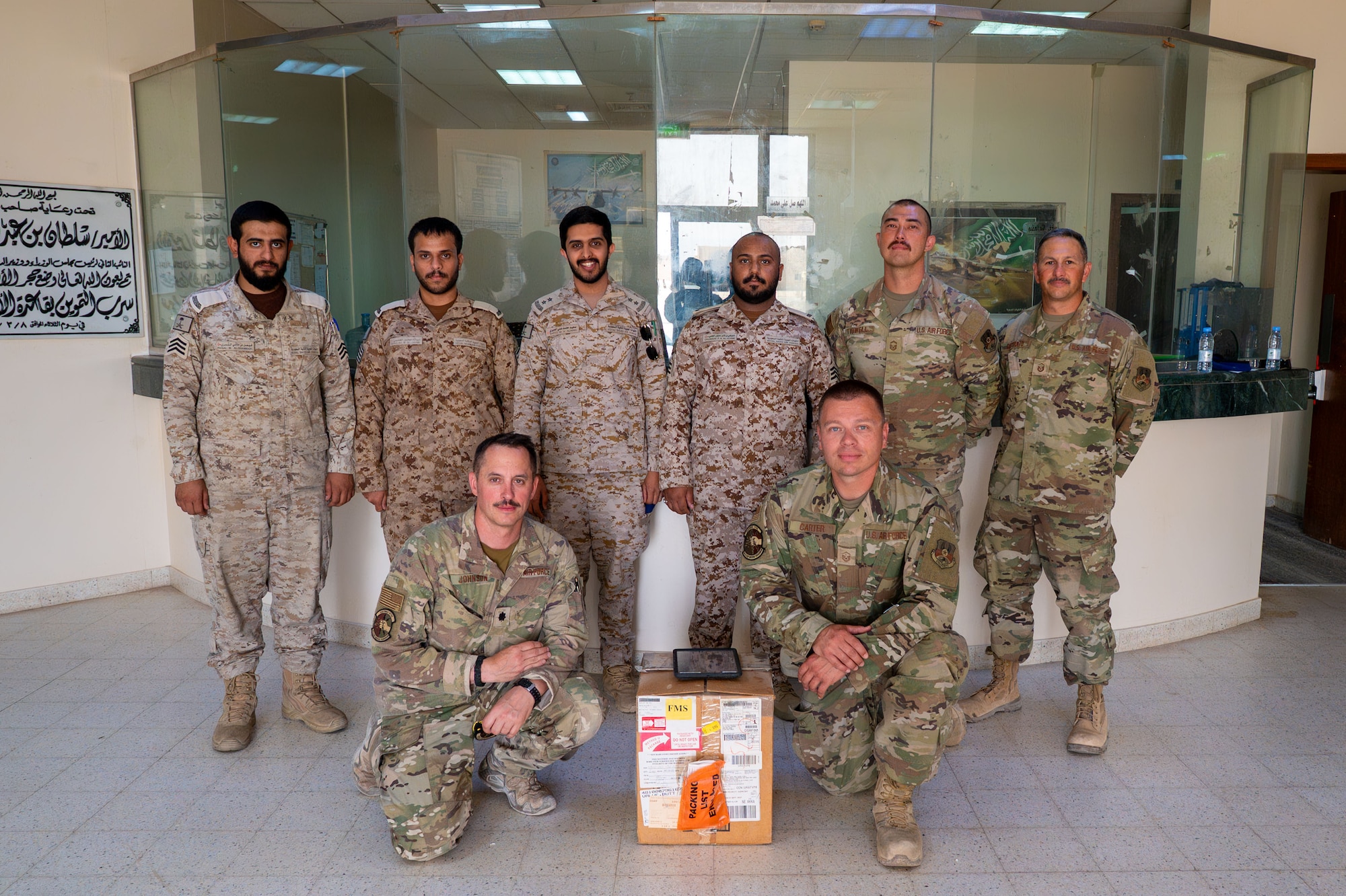 Four U.S. Air Force and four Royal Saudi Air Force service members pose for a photo with a box.