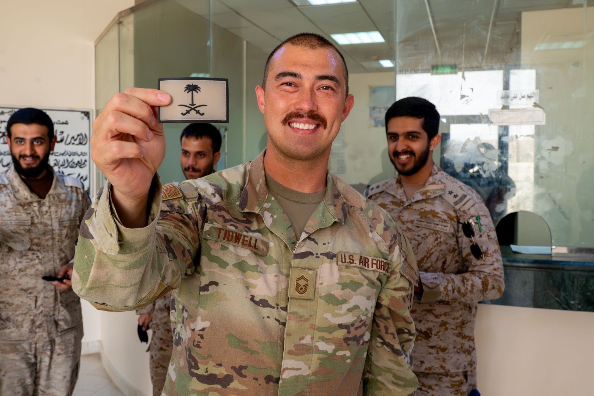 A U.S. Air Force servicemembers smiles for a photo while holding a Royal Saudi Air Force patch.