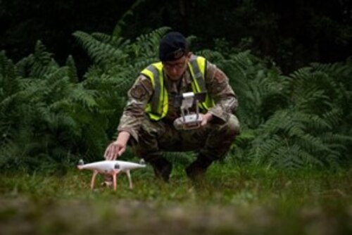 A U.S. Air Force Airman sets up a drone in a wooded area.