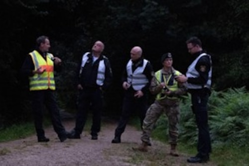 U.S. Air Force and German Polizei members stand on a dirt road talking to each other.