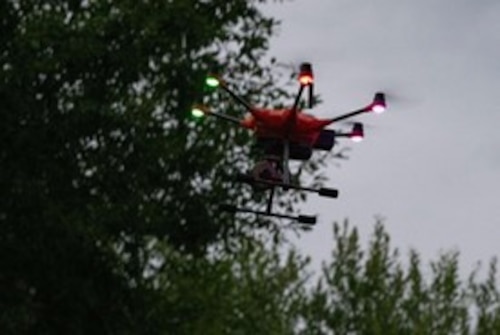 A drone flies near trees at dusk.