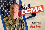 A man wears an Army camouflage uniform and stands near the American flag