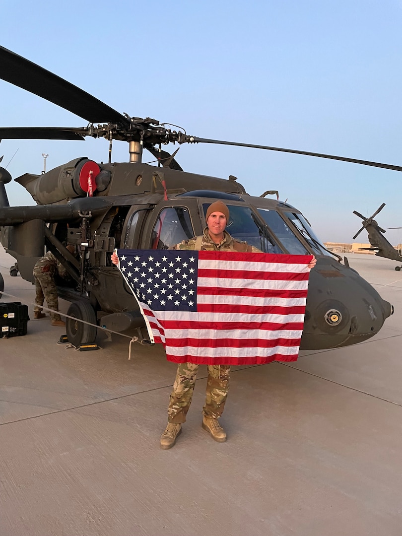 An Army pilot stands in front of a Black Hawk holding the American flag