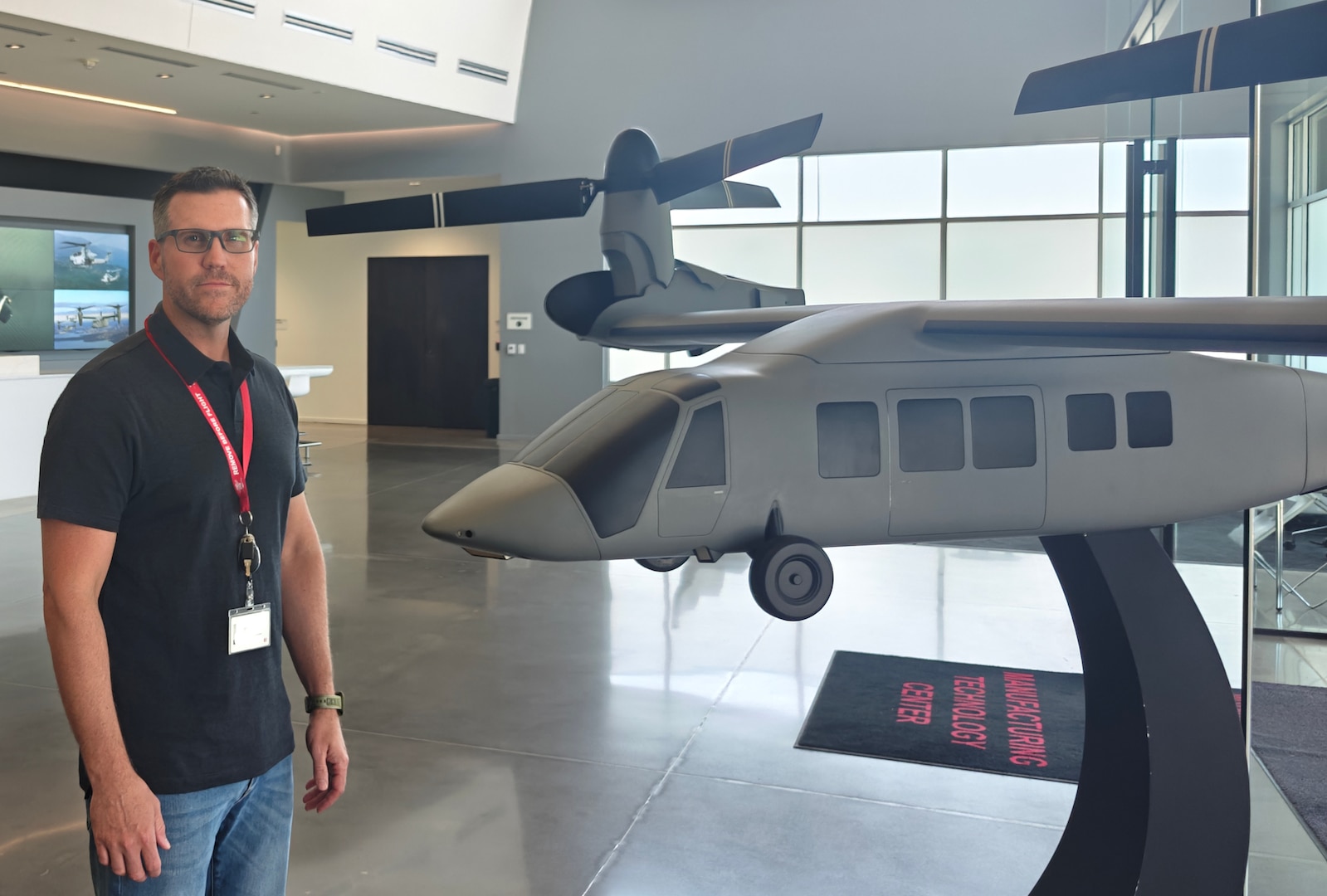 A man wearing a black shirt and blue jeans stands beside aircraft in a building