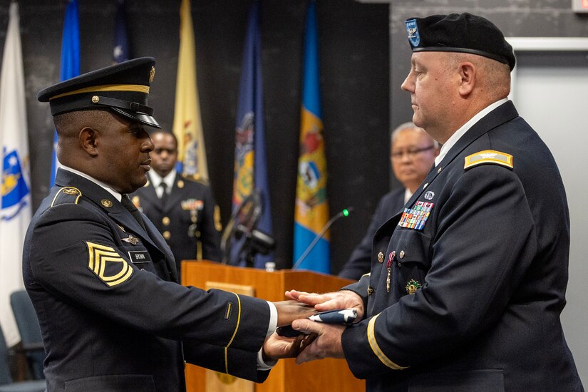 Sgt. 1st Class Deterrance Brown, U.S. Army Financial Management Command senior FM systems instructor, presents an American Flag to Col. Ralph M. “Mac” Crum, USAFMCOM finance officer, during Crum’s retirement ceremony at the Maj. Gen. Emmett J. Bean Federal Center in Indianapolis Nov. 26, 2024. Crum most recently served as USAFMCOM’s chief of staff and served four combat tours during his career. (U.S. Army photo by Brad Staggs)