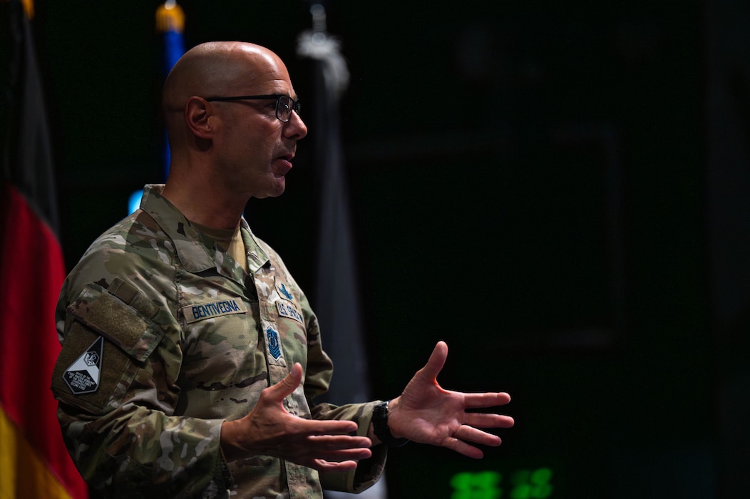 The Chief gestures to the audience while on stage in an auditorium