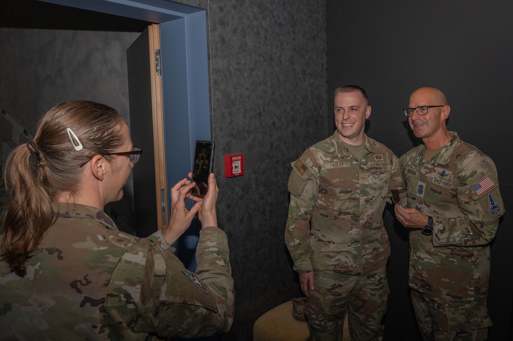 The Chief holds up a patch given to him by an Airman in an auditorium