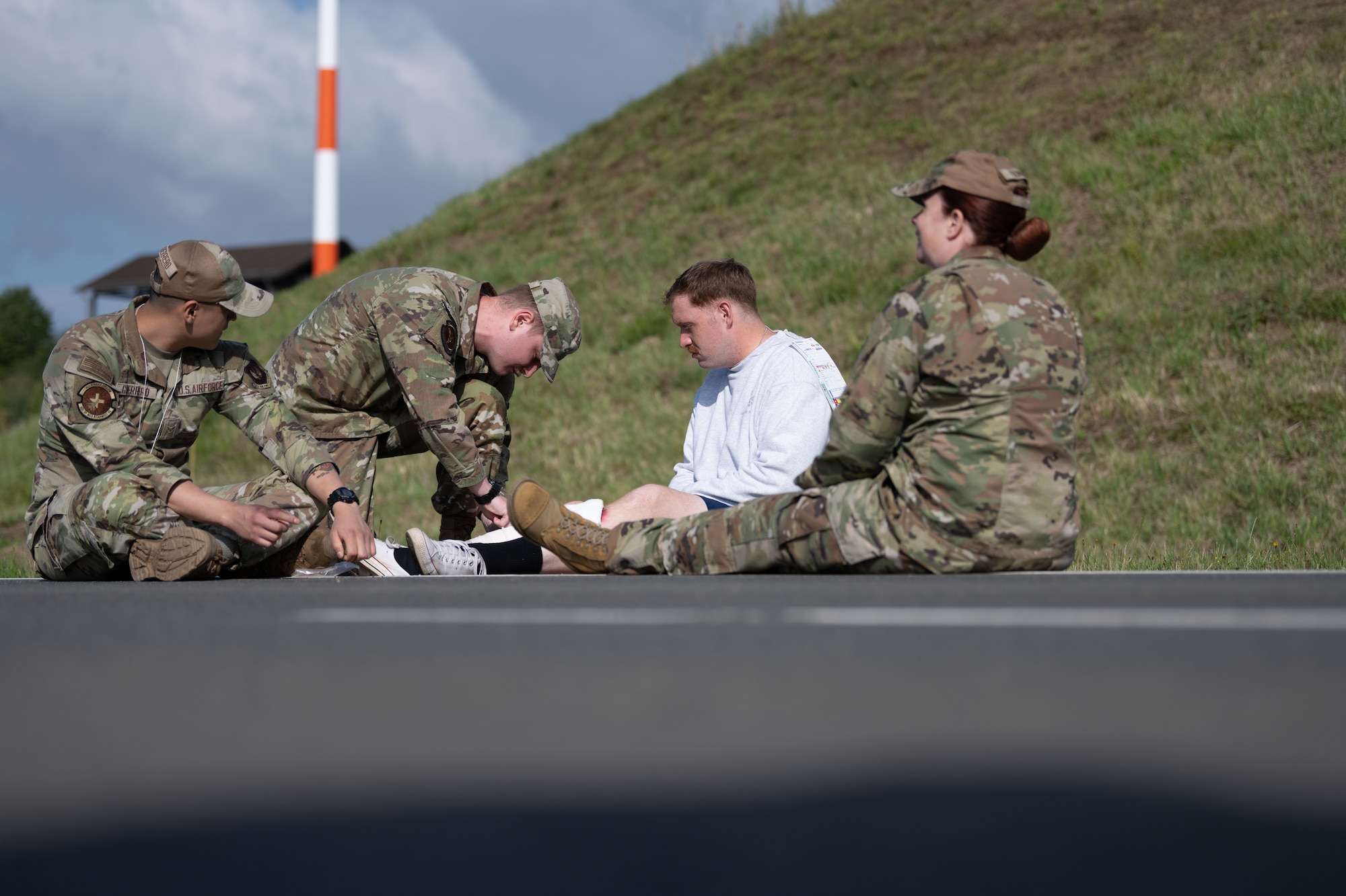 U.S. Air Force Airman 1st Class Jacob Parker, 52nd Medical Group medical technician, center left, treats a simulated wound on Airman 1st Class Daniel Hartley, center right, 52nd MDG pediatrics technician, during a Major Accident Response Exercise, July 30, 2025. The MARE is a means for the Wing Inspection Team to assess and evaluate how first responders react to realistic emergency scenarios.