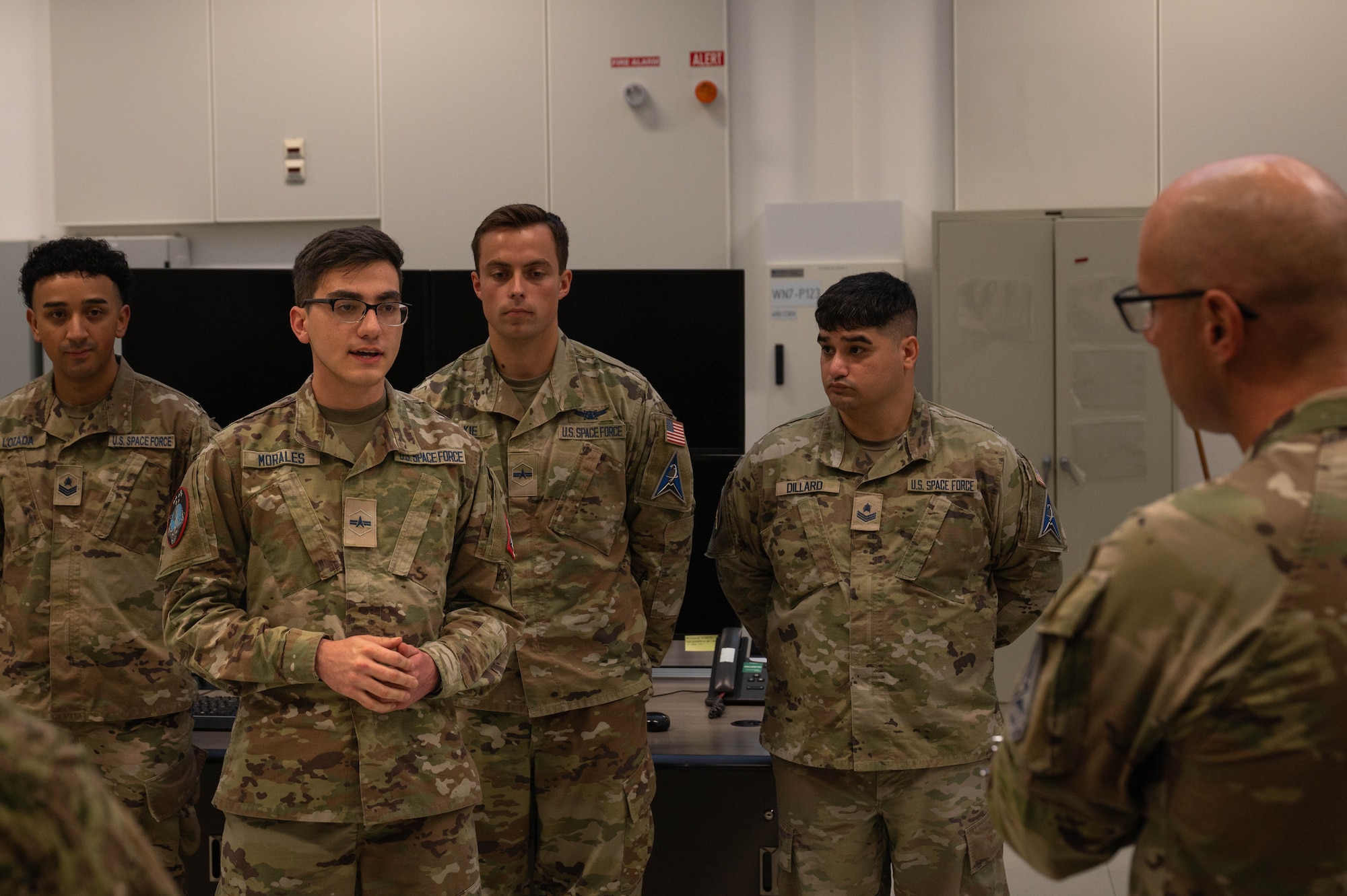 A young Guardian speaks to the Chief in front of his peers at an office-like work center