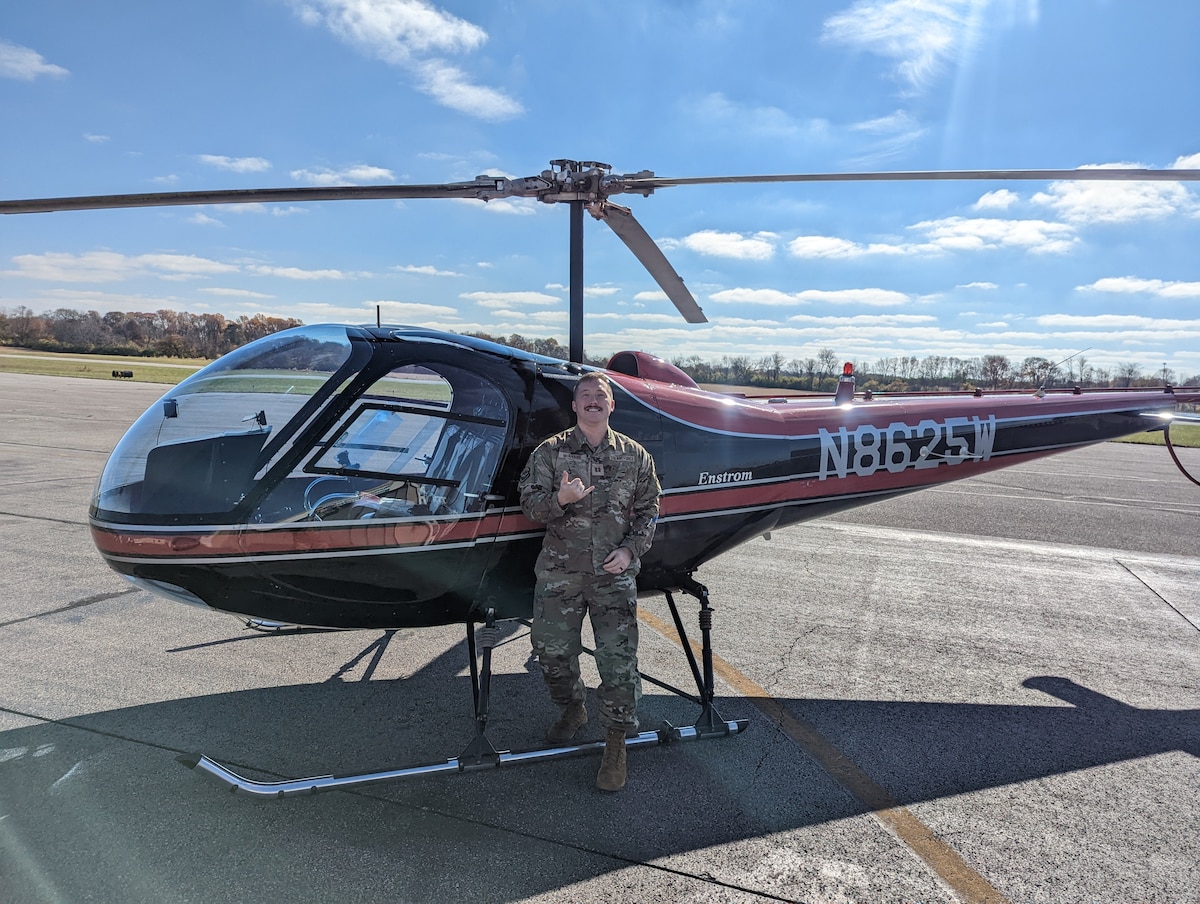 Image of an Airman posing for a photo in front of a helicopter.