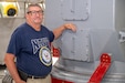 A person wearing a United States Navy t-shirt poses for a photo next to a military asset.
