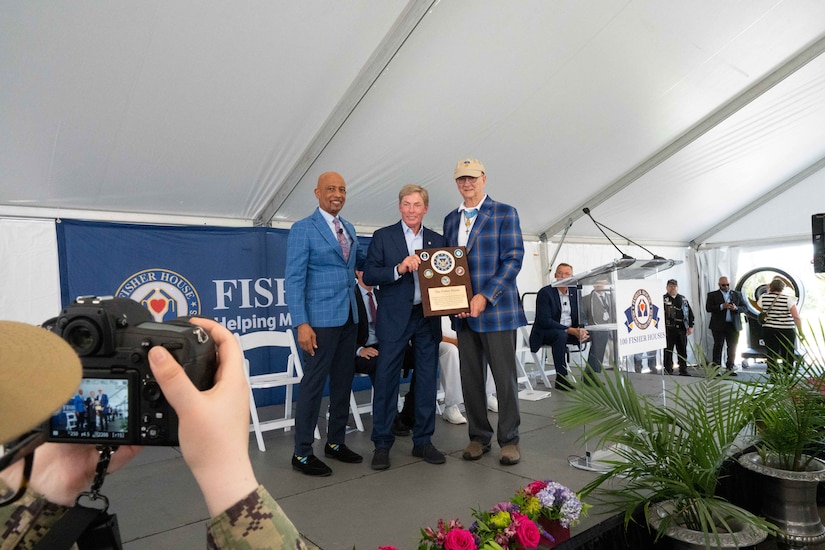 Three men in business clothing stand together on a stage and hold a plaque up for a photo.