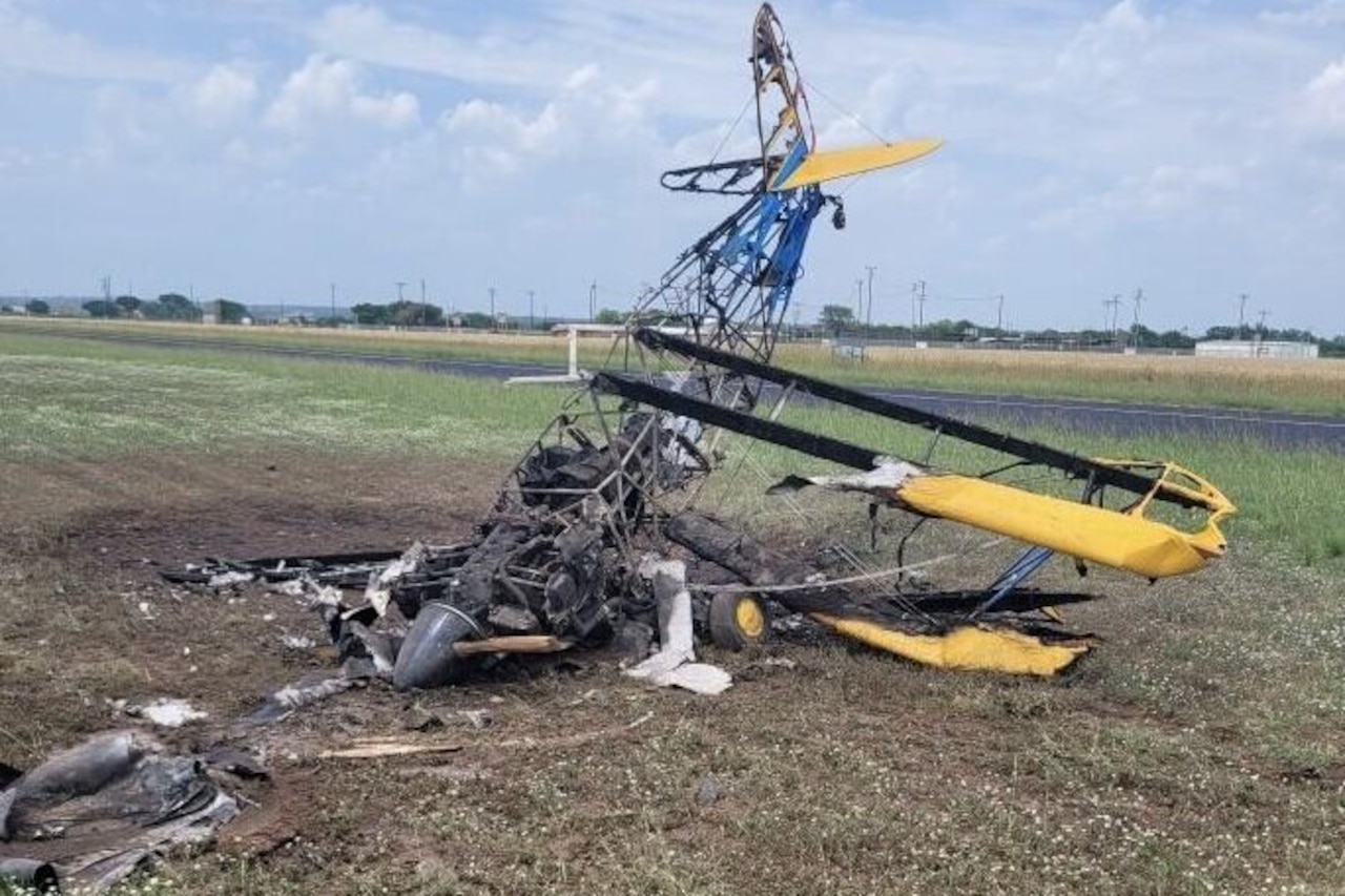 A plane's burned skeleton standing on its nose lays in a grass field.