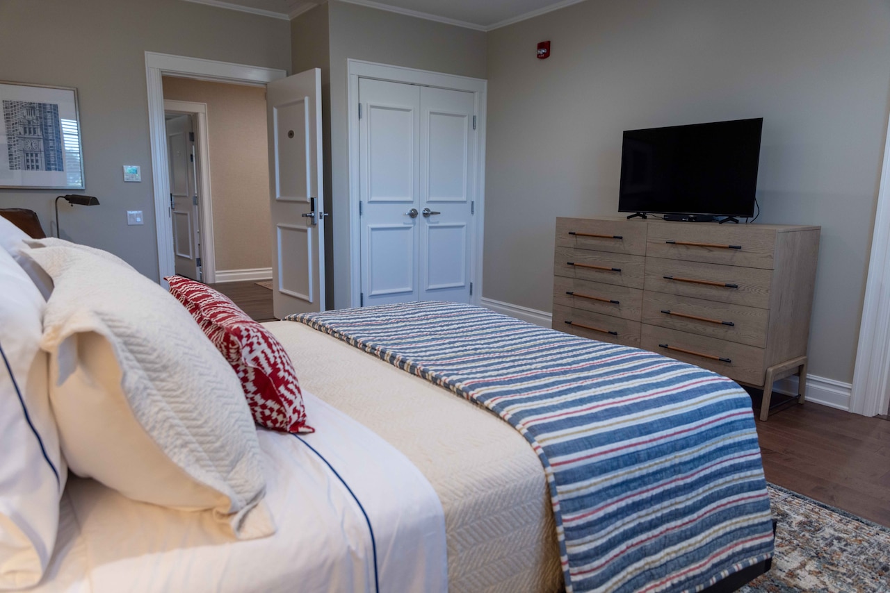 A large bed, a set of dressers and a TV sit in a room with a closet.
