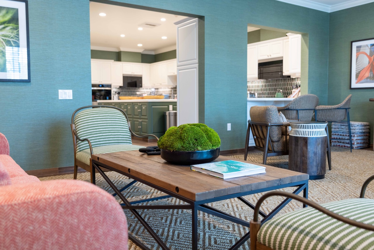 A spacious living room is shown with doors and windows looking into a large kitchen.