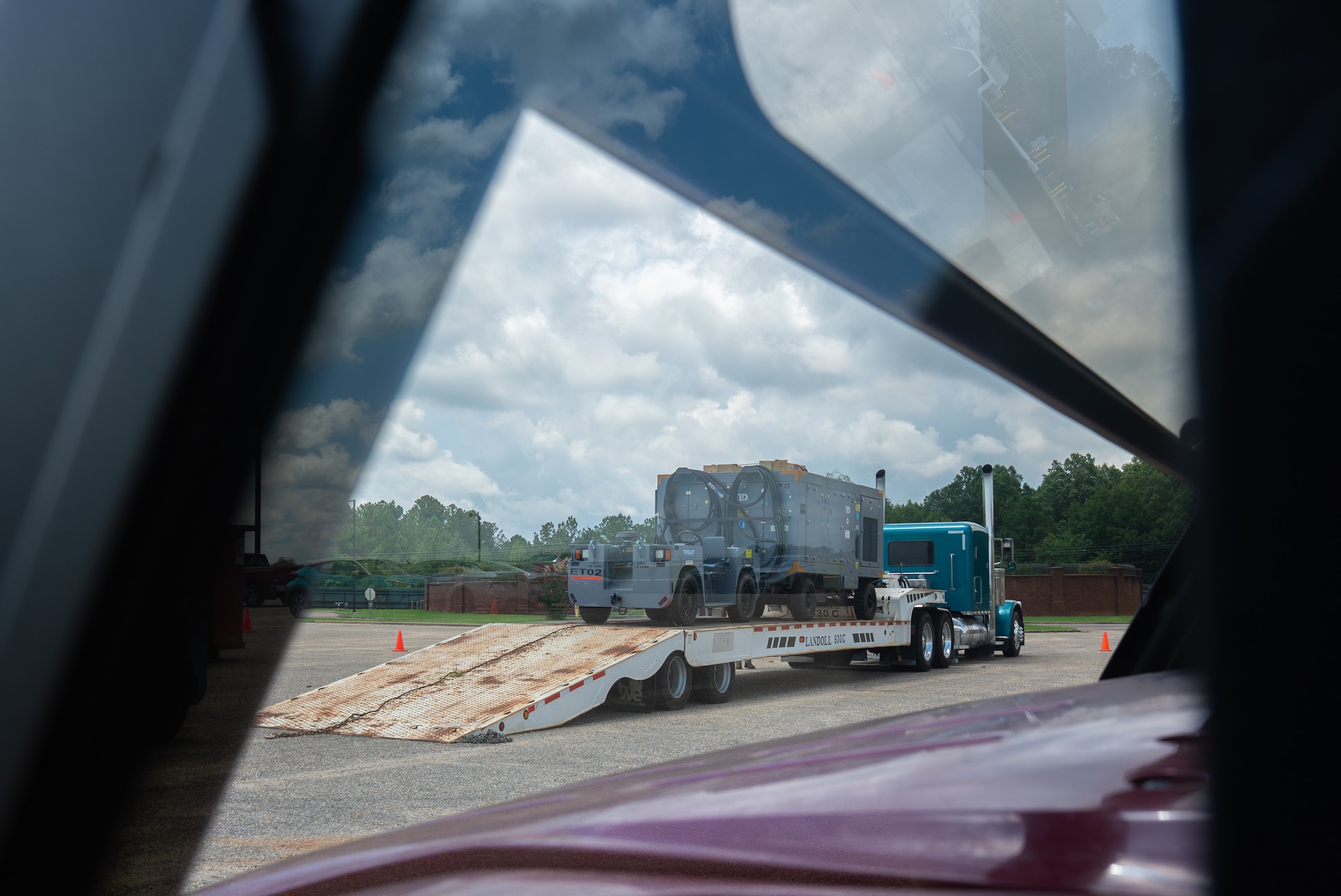U.S. Airmen with the 187th Fighter Wing, Alabama Air National Guard, finalize preparations for a loaded semitruck to depart, seen through the windshield of a utility vehicle at Dannelly Field, Alabama, July 2, 2025. The operation is in support of the first-in-a-generation Department-Level Exercise series, a new way of conducting operations in a contested, dynamic environment to build capabilities making a stronger, more lethal deterrent force. The DLE series encompasses all branches of the Department of Defense, along with Allies and partners, employing more than 400 Joint and coalition aircraft and more than 12,000 members at more than 50 locations across 3,000 miles. (U.S. Air National Guard photo by Airman 1st Class Andre Bordlee)
