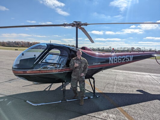 Image of an Airman posing for a photo in front of a helicopter.