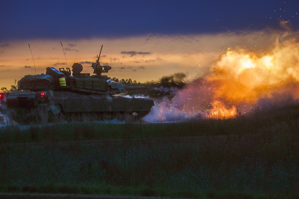 A tank fires in a field creating a smoky fireball under dark sky with orangish hues.