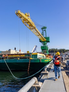 Carlos Murphy, rigger, Code 740, Riggers, helps guide a barge carrying new portal Crane 52 into Pier Bravo at Puget Sound Naval Shipyard & Intermediate Maintenance Facility in Bremerton, Washington. July 14, 2025. (U.S. Navy photo by Wendy Hallmark)