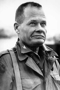A man in uniform without a head cover on looks up into the distance.