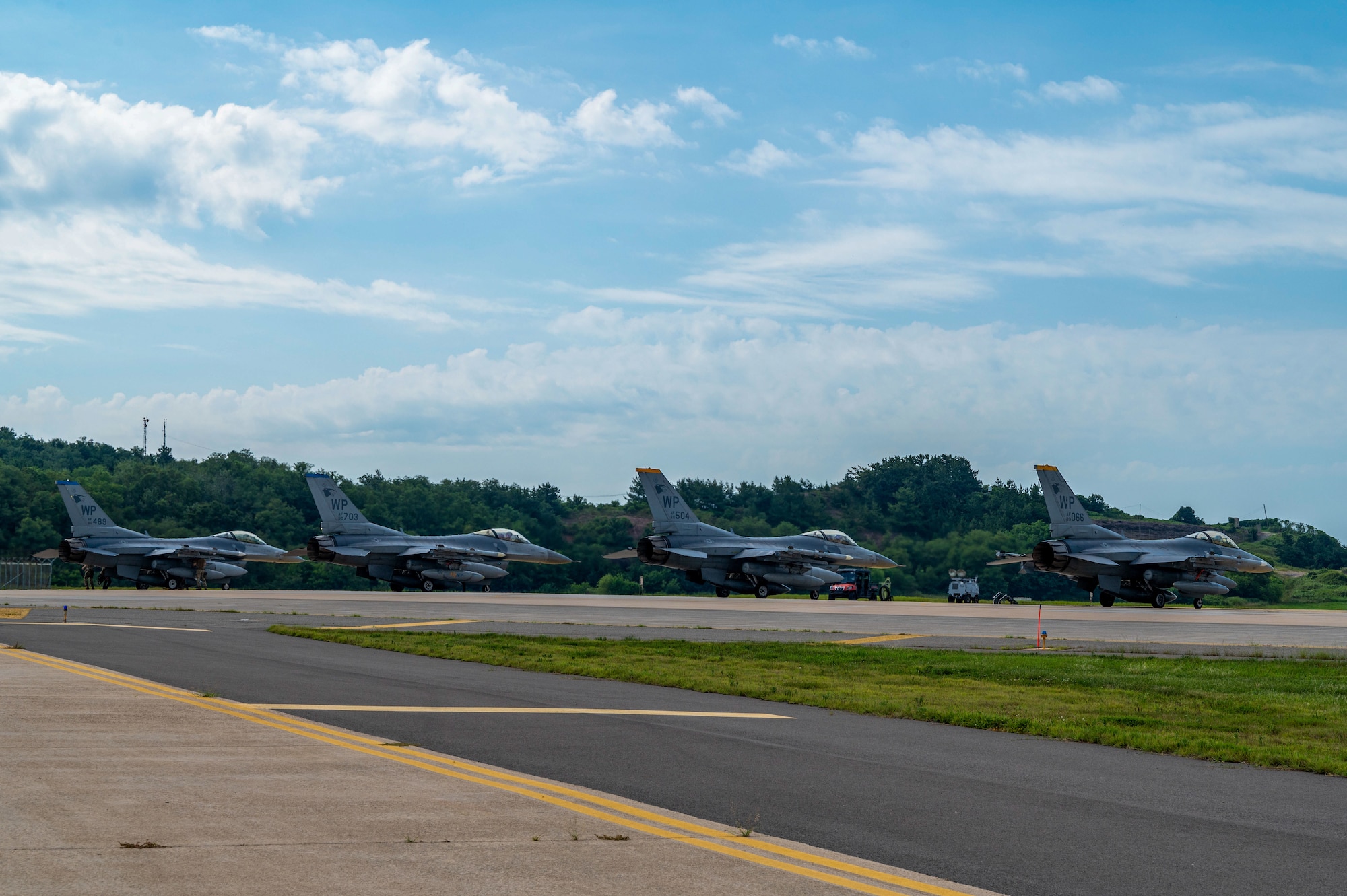 A group of F-16 Fighting Falcon aircraft sit on a runway prior to takeoff